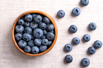 Blueberries in a wooden bowl on linen fabric. Dark blue colored, ripe, raw berries, fruits of Vaccinium corymbosum, cultivated blueberries of the northern highbush blueberry. From above, food photo.