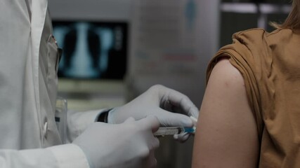 Closeup of hands of unrecognizable doctor in protective gloves sterilizing injection site with alcohol and doing vaccination to patients shoulder in modern hospital
