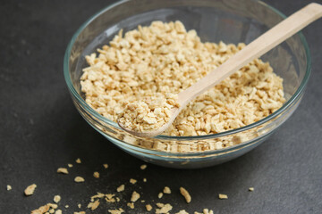 Close up of dried soy bean meat mince in a glass bowl with a wooden spoon, grey table