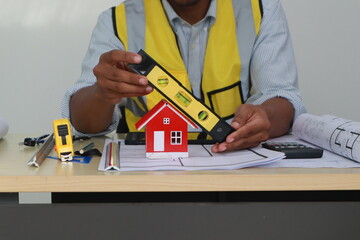 An engineer meticulously draws house plans on a workbench, surrounded by tools and blueprints,...