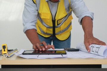 An engineer meticulously draws house plans on a workbench, surrounded by tools and blueprints,...