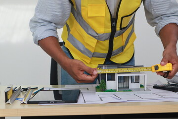 An engineer meticulously draws house plans on a workbench, surrounded by tools and blueprints,...