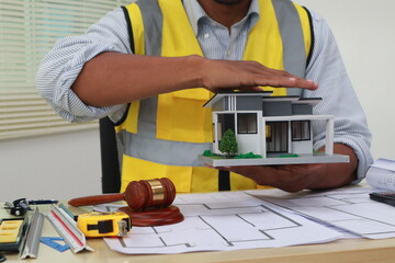 An engineer meticulously draws house plans on a workbench, surrounded by tools and blueprints,...