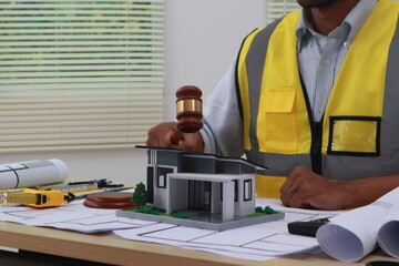 An engineer meticulously draws house plans on a workbench, surrounded by tools and blueprints,...