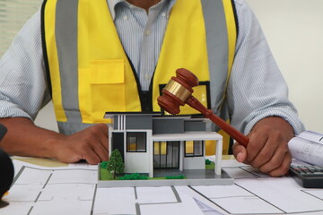 An engineer meticulously draws house plans on a workbench, surrounded by tools and blueprints,...