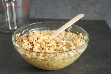 Close up of soy bean meat mince sucked up in water in a glass bowl with a wooden spoon, grey kitchen table