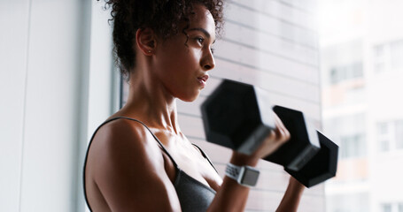 African woman, dumbbells and training for fitness with thinking, wellness and muscle development in gym. Person, bodybuilder and weightlifting by window, workout and challenge for transformation