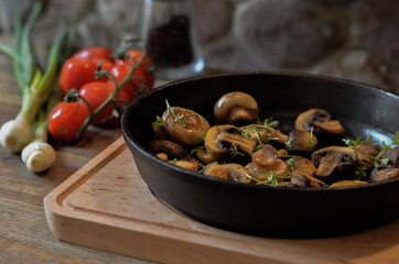 Fried mushroom, champignon, in pan on wood table, vegetables in background.