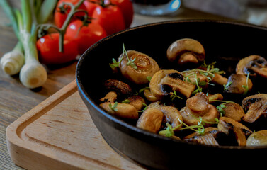 Fried mushroom, champignon, in pan on wood table, vegetables in background.