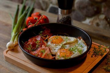 Fried eggs with bacon in a pan on a wooden table