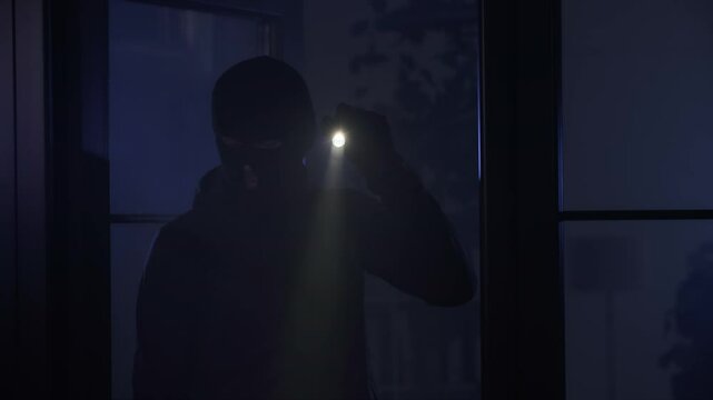 crime and criminality, man in a balaclava illuminates a room with a flashlight in search of valuables