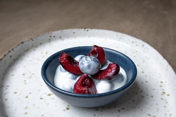 Fresh summer cherries with a dish of blueberries and yogurt on a teardrop shaped platter on a stone worktop