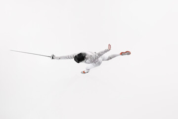 Overhead view of fencer with their rapier extended and one leg kicked up for balance against white...