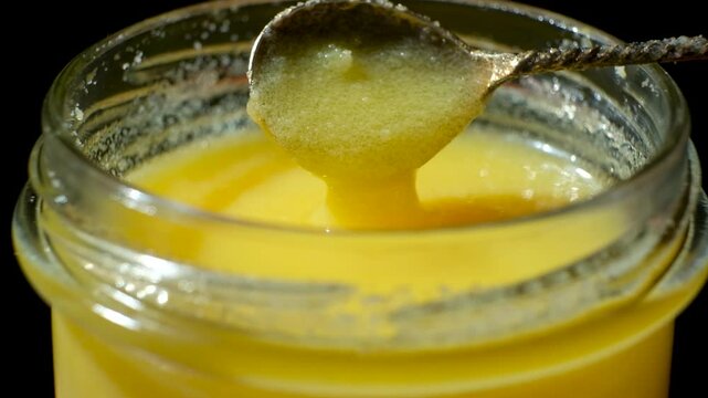 Fresh ghee oil pouring from spoon into jar, slow motion