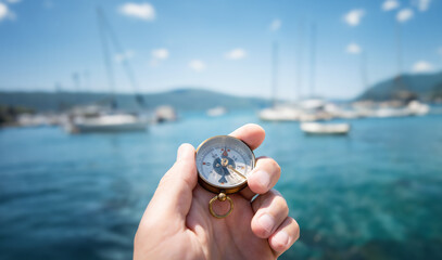 Compass in hand on the background of yachts and the sea. Background on the theme of travel, navigation, voyage, hike, etc. Shallow depth of field, sharpness on the compass.