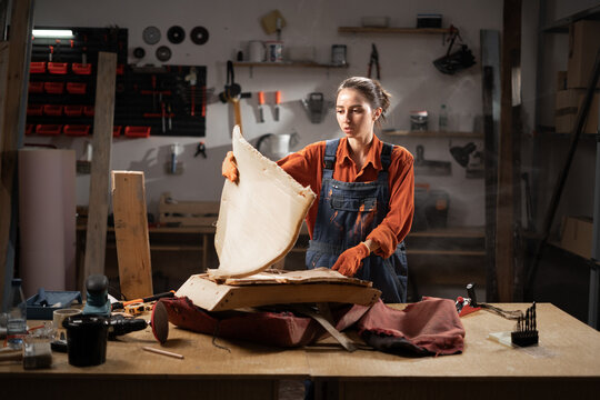 Woman in workshop restoring antique furniture disassembling old armchair into parts for refurbishment focusing on updating and renewing vintage pieces with craftsmanship.