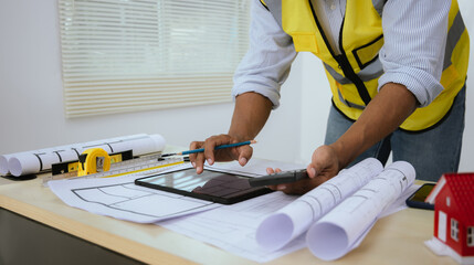 Male architect working at table with toy house model and A3 paper blueprints. Real estate...