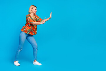 Photo of cute cheerful girl wear stylish orange print clothes push big empty space isolated on blue color background