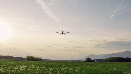 Airplane flying over the beautiful blossom meadow at sunset. Travel, vacation, and freedom concepts.