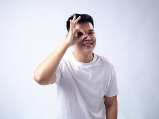 A young Asian man, wearing a white shirt and black watch, makes a playful expression while forming an 