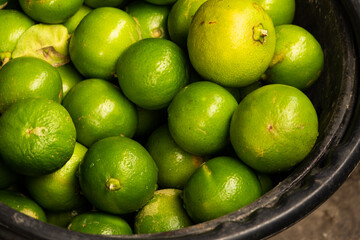A bunch of green limes in a black bowl. The limes are all different sizes and are piled on top of each other