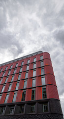 Low angle detail of the facade of the Ilona Rose House development on Charing Cross Road, London under a white sky with cobwebs of clouds backlit by the setting sun.