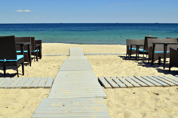 tables and a wooden walkway to the sea. A wooden walkway leading from the beach to the sea with a...