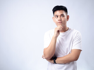 A young Asian man, wearing a white shirt and black watch, looks pensively to the side while resting his chin on his hand. The plain white background emphasizes the subject's contemplative