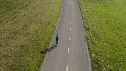 Racing cyclist riding on an empty flat asphalt road, aerial top down drone shot.