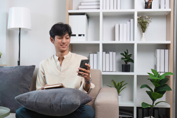 Young Man Relaxing in Modern Living Room with Smartphone and Book, Surrounded by Minimalist Decor and Indoor Plants