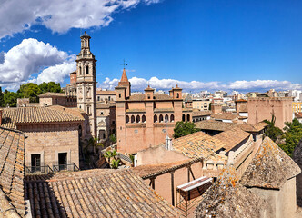 Panoramic view of the Pueblo Español Open-air Museum of Architecture, featuring traditional Spanish buildings with terracotta roofs, a bell tower, and an urban cityscape under a blue sky with clouds