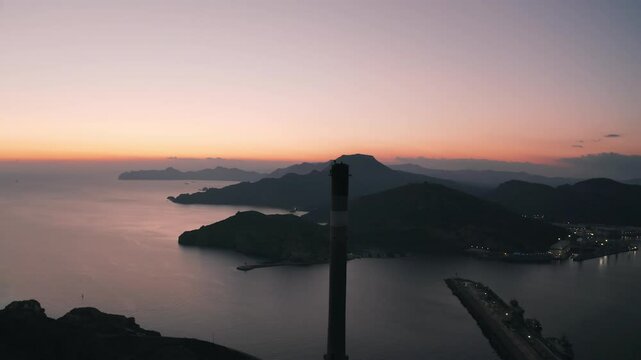 Aerial parallax right shot of 3 people standing on topo of an old abandoned chimney overlooking at some mountains and the sea at sunset in Cartagena, Spain Chimenea de Pe&ntilde;arroya