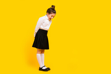 Full size photo of cute schoolgirl look down empty space ad wear uniform isolated on yellow color background © deagreez