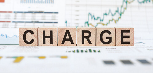Wooden blocks spelling the word charge on a table with financial charts in the background.