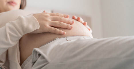 Pregnant asian woman holds hands on belly touching her baby caring about her health Beautiful happy pregnant woman tender mood photo of pregnancy