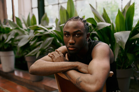 Handsome African American man with sophisticated dapper style sitting in a chair with arms crossed in a vibrant green garden.