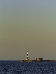 Isolated lighthouse and cottage on a rocky island, standing sentinel against the tranquil sea,...