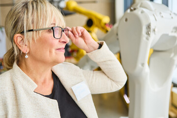 Woman adjusting glasses while observing robotics training and programming in industry setting