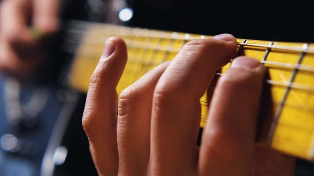Close-up of a hand playing an electric guitar, with sharp emphasis on the fingers pressing the strings on the maple fingerboard. Male fingers playing a guitar solo