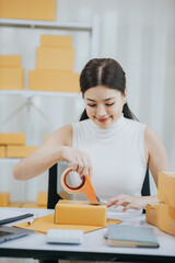Young Asian entrepreneur running an online business from home Manage online orders and shipping packages She markets the product. Manage inventory and delight customers using laptops and smartphones.