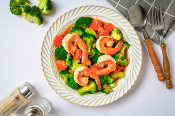 Stir fried broccoli with shrimp in a white ceramic plate witn spoon and fork on white table background