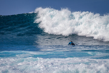 Naklejka premium Tenerife, Spain 02 11 2013: Young man surfing on a big wave with white foam. Blue sky. Surfing day. Atlantic Ocean. Tenerife, Canary Islands, Spain.