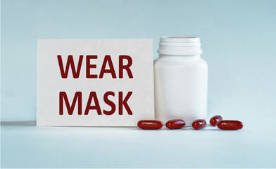 White Pill Bottle With Red Capsules and a Sign Reading Wear Mask