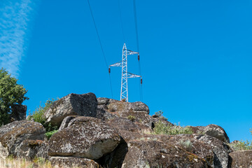 Fototapeta premium Poste elétrico de alta tensão no alto de um monte rochoso sob um céu azul