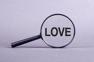 A magnifying glass hovering over the word love on a neutral background.