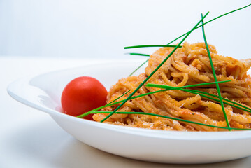 Spaghetti with tomato sauce and chives on a white plate.