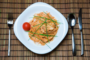 Spaghetti with tomato sauce and chives on a white plate.