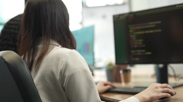 Female Software Developer Writing Code in Modern Office, Rear View of Woman Programmer Working on Computer with Code Displayed on Monitor, Professional Technology Workspace Environment.