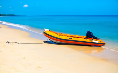 An inflatable motor boat is moored with an anchor on the sandy seashore.