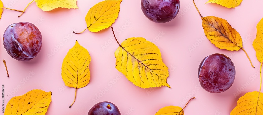 Poster top view of a fall-themed flat lay with yellow leaves and plum on a light pink background, providing